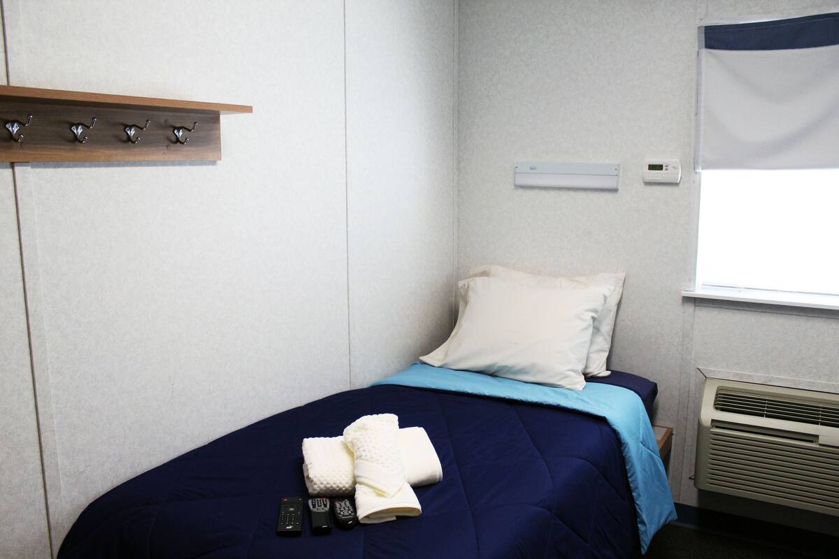 Een net opgemaakt bed met een blauw-witte dekbedovertrek, een houten plank erboven en een wit kussen.