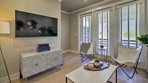 A modern living room with a large flat-screen TV, a white console table, two chairs, and a coffee table.