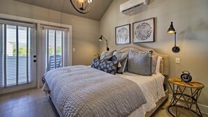 A bedroom with a large bed, a ceiling light, an air conditioner, and a small table with a clock.