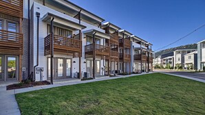 A row of modern townhouses with balconies, a well-maintained lawn, and a clear blue sky.