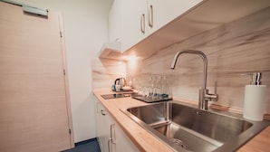 A modern kitchen with a stainless steel sink, wooden countertop, and white cabinets. - Villa Centro (Oswiecim)