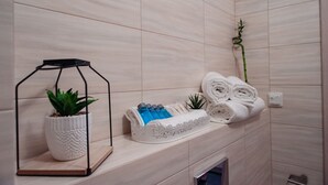 A bathroom with a wooden shelf holding a potted plant, a set of toiletries, and rolled towels. - Villa Centro (Oswiecim)