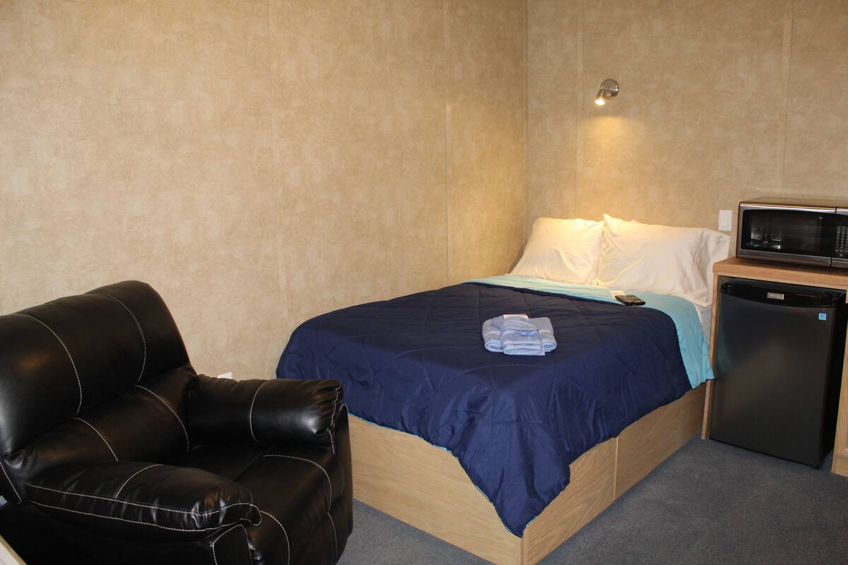 A bedroom with a bed, a black leather chair, a microwave, and a small refrigerator.
