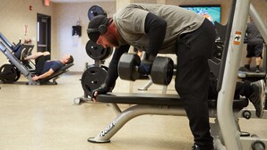 Une salle de sport équipée de matériel de musculation et une personne effectuant un développé couché.