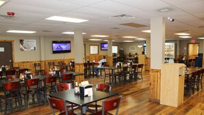Un restaurant doté de nombreuses tables et chaises, d’un plancher en bois et d’un téléviseur fixé au mur.