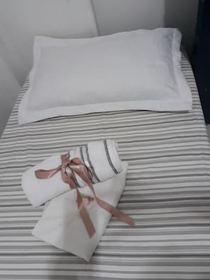 A bed with a striped bedspread and a neatly folded white garment with a ribbon tied around it. - Pousada Executiva (Teresina)