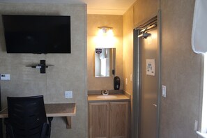 A compact bathroom with a sink, mirror, and a television mounted on the wall. - Target Hospitality-Seven Rivers Lodge Carlsbad (Carlsbad)