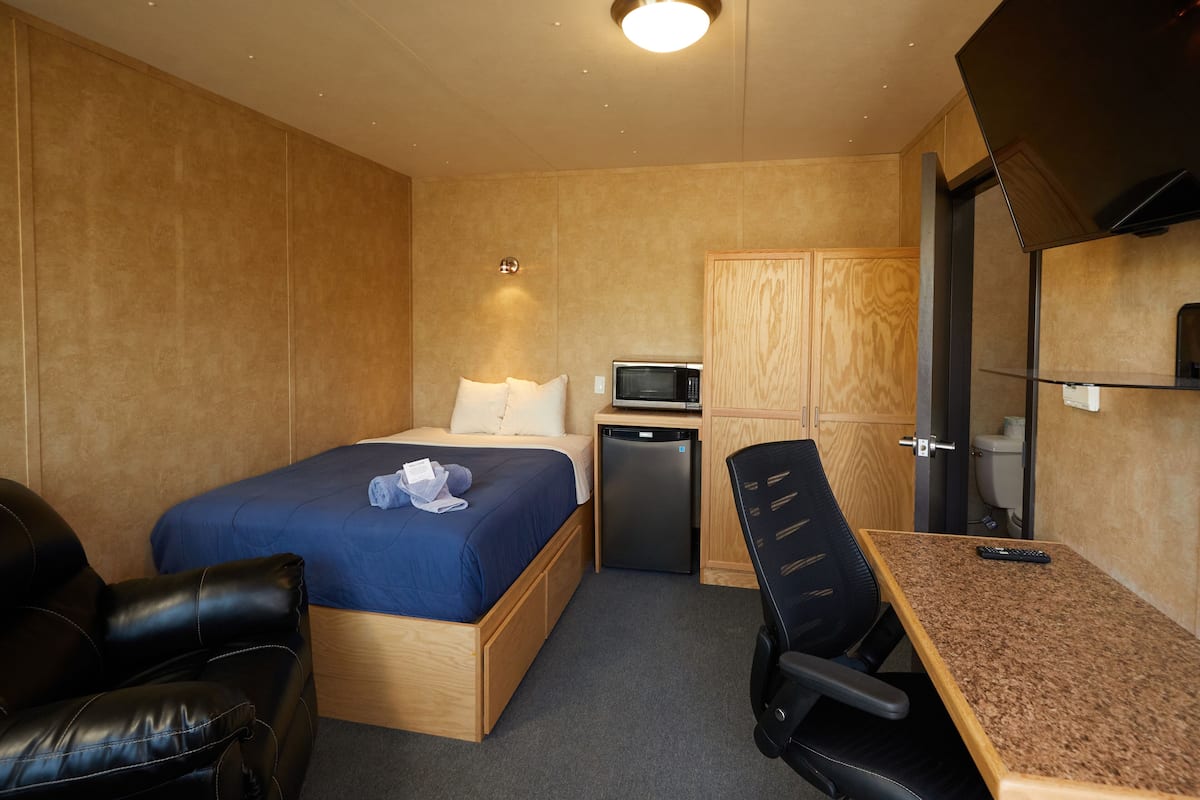 A compact hotel room with a bed, a desk, a chair, a microwave, and a small refrigerator.