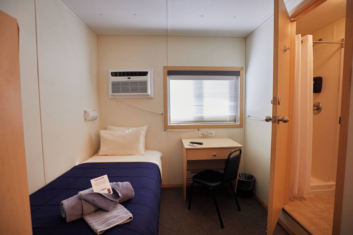 A compact hotel room with a single bed, a desk, a chair, and a shower.