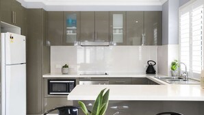Una cocina moderna con electrodomésticos de acero inoxidable, una encimera blanca y un ventanal con persianas.