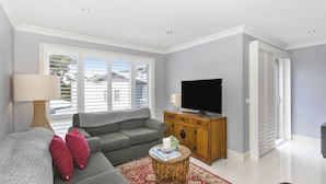 Una sala de estar con un sofá gris, un mueble de madera con un televisor, una lámpara y una alfombra roja.