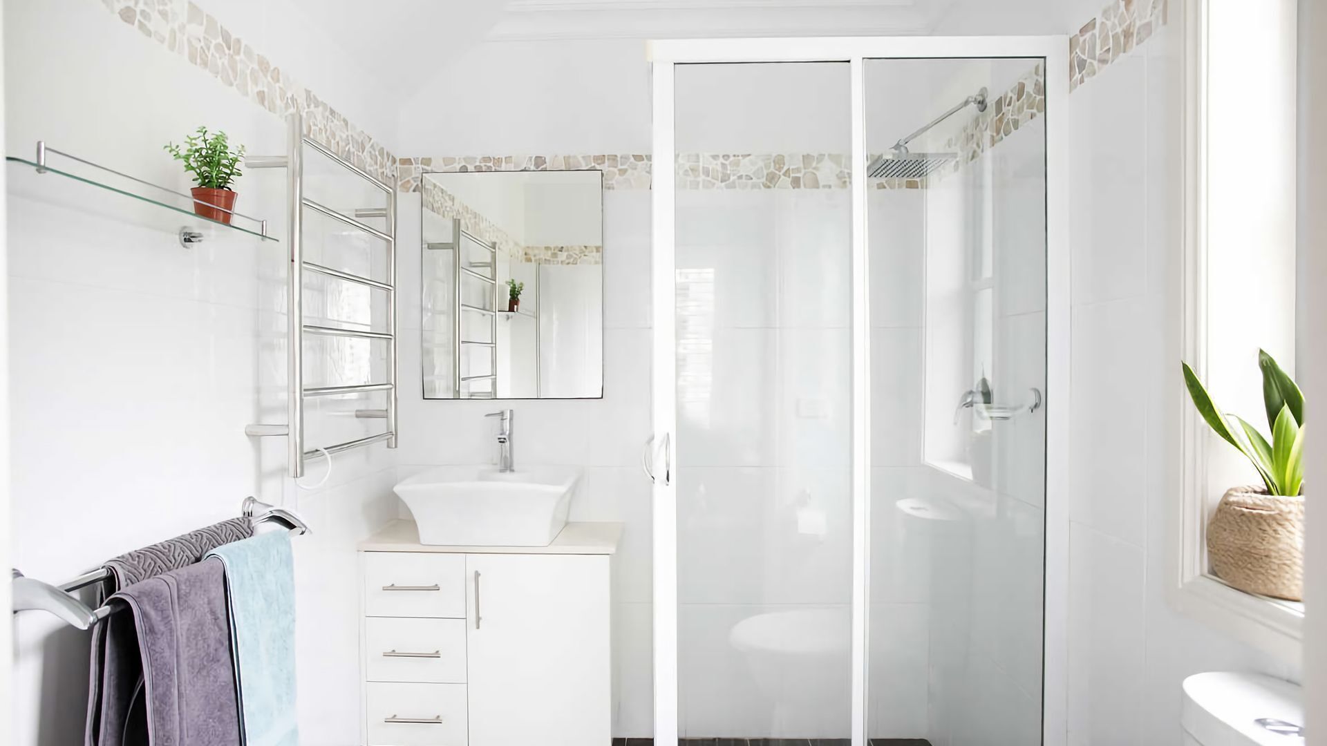 Un baño moderno con cabina de ducha de vidrio, un lavamanos blanco y un espejo sobre el mueble.