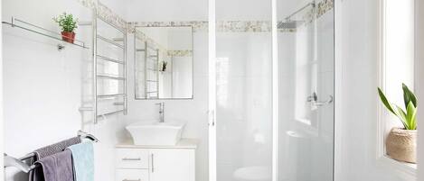 Un baño moderno con cabina de ducha de vidrio, un lavamanos blanco y un espejo sobre el mueble.