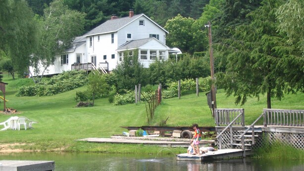 A house with a dock extending into a calm lake, surrounded by lush greenery.