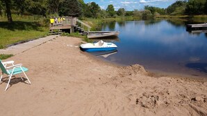A sandy beach with a dock, a rowboat, and a chair.