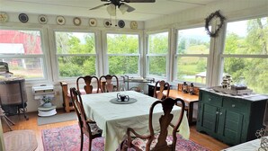A dining room with a table set for six, surrounded by wooden chairs, a patterned rug, and a view of greenery outside.