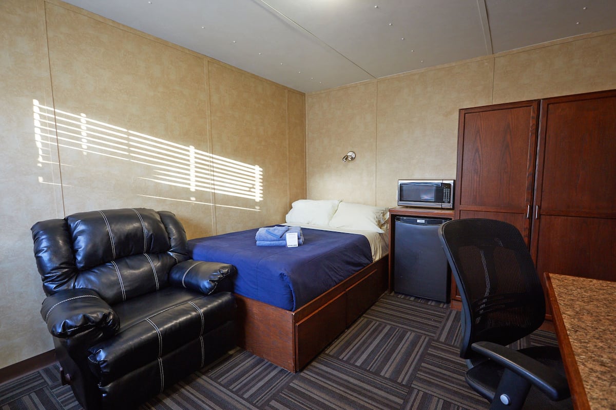 A hotel room with a bed, a leather sofa, a desk with a computer, and a microwave.