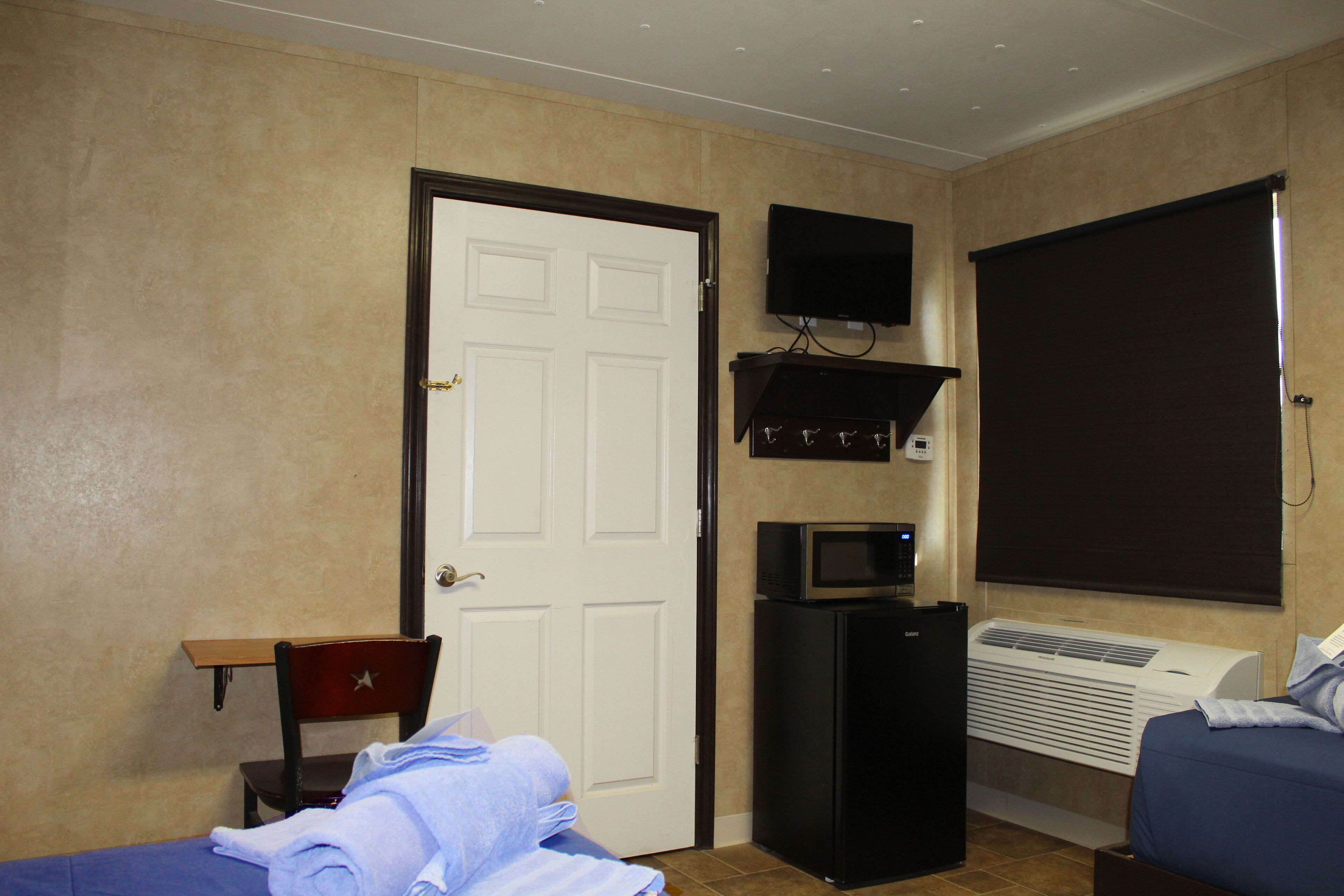 A hotel room with a bed, a chair, a desk, a television, and an air conditioning unit.