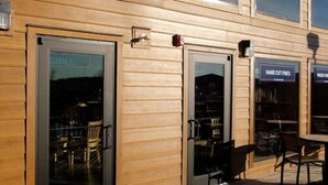 Un restaurant avec une terrasse, une enseigne indiquant qu’il propose des grillades et une autre indiquant qu’il sert des frites coupées à la main.
