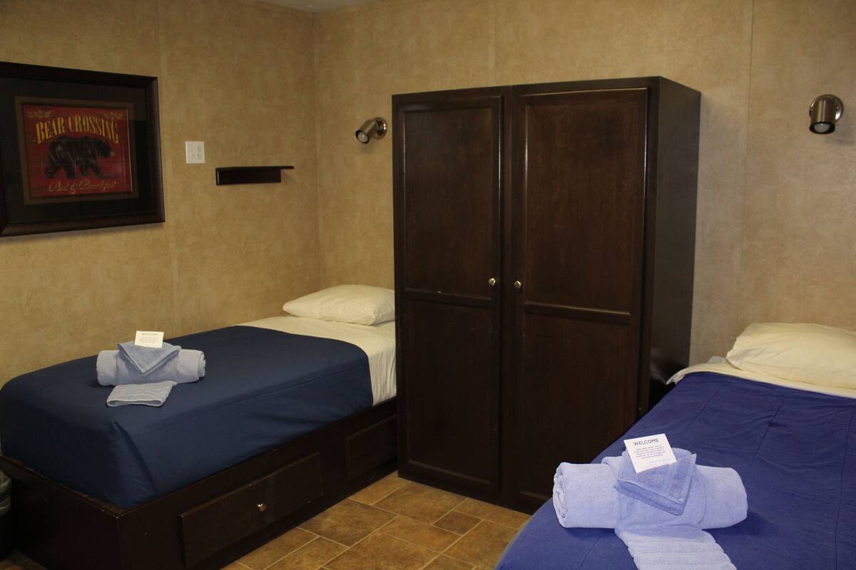 A hotel room with two beds, a wardrobe, a framed picture on the wall, and a welcome sign.
