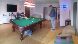 A pool table in a room with a billiard cue, a television mounted on the wall, and a neon sign.