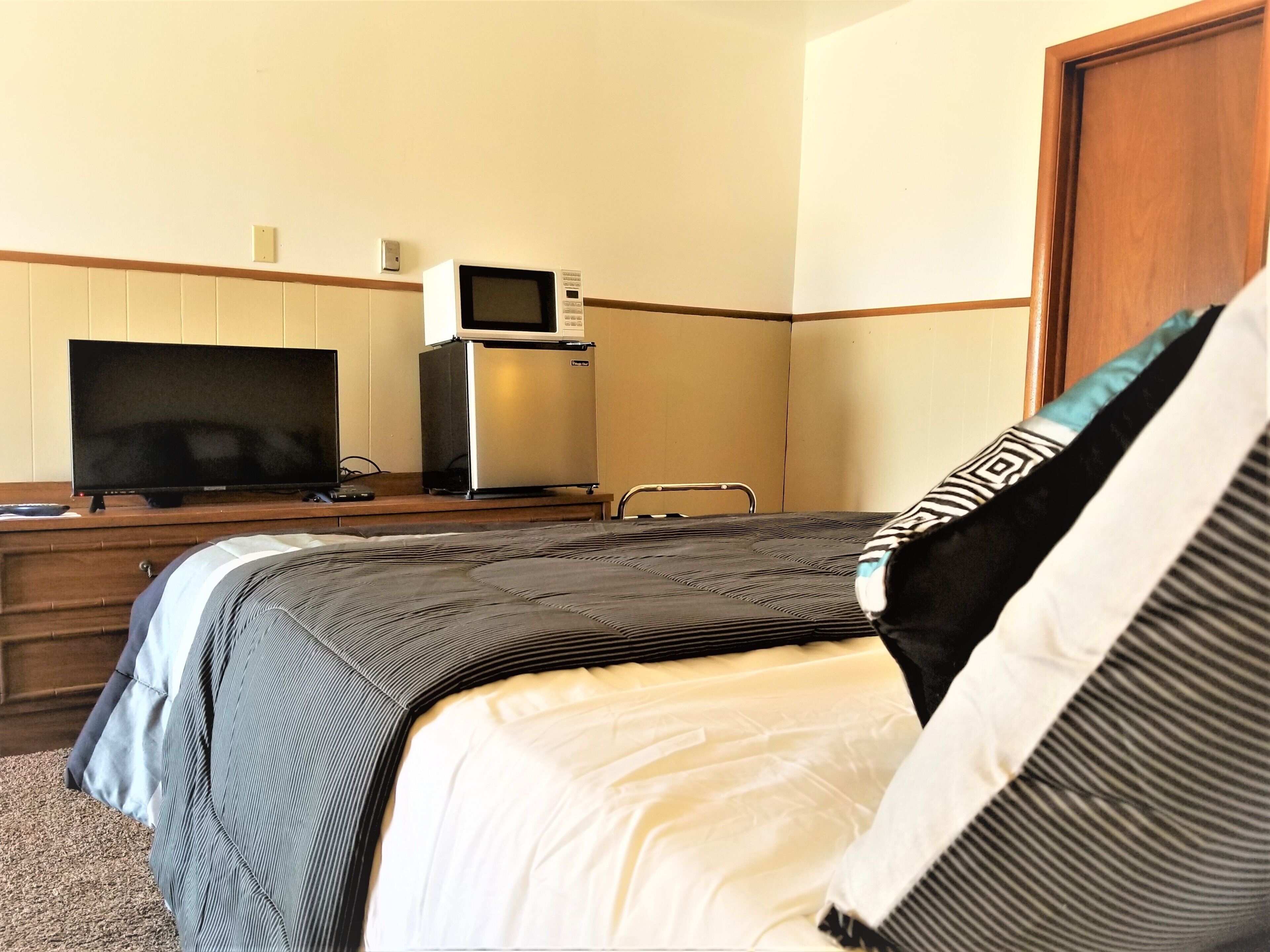 A hotel room with a bed, a television, a microwave, and a wooden desk.