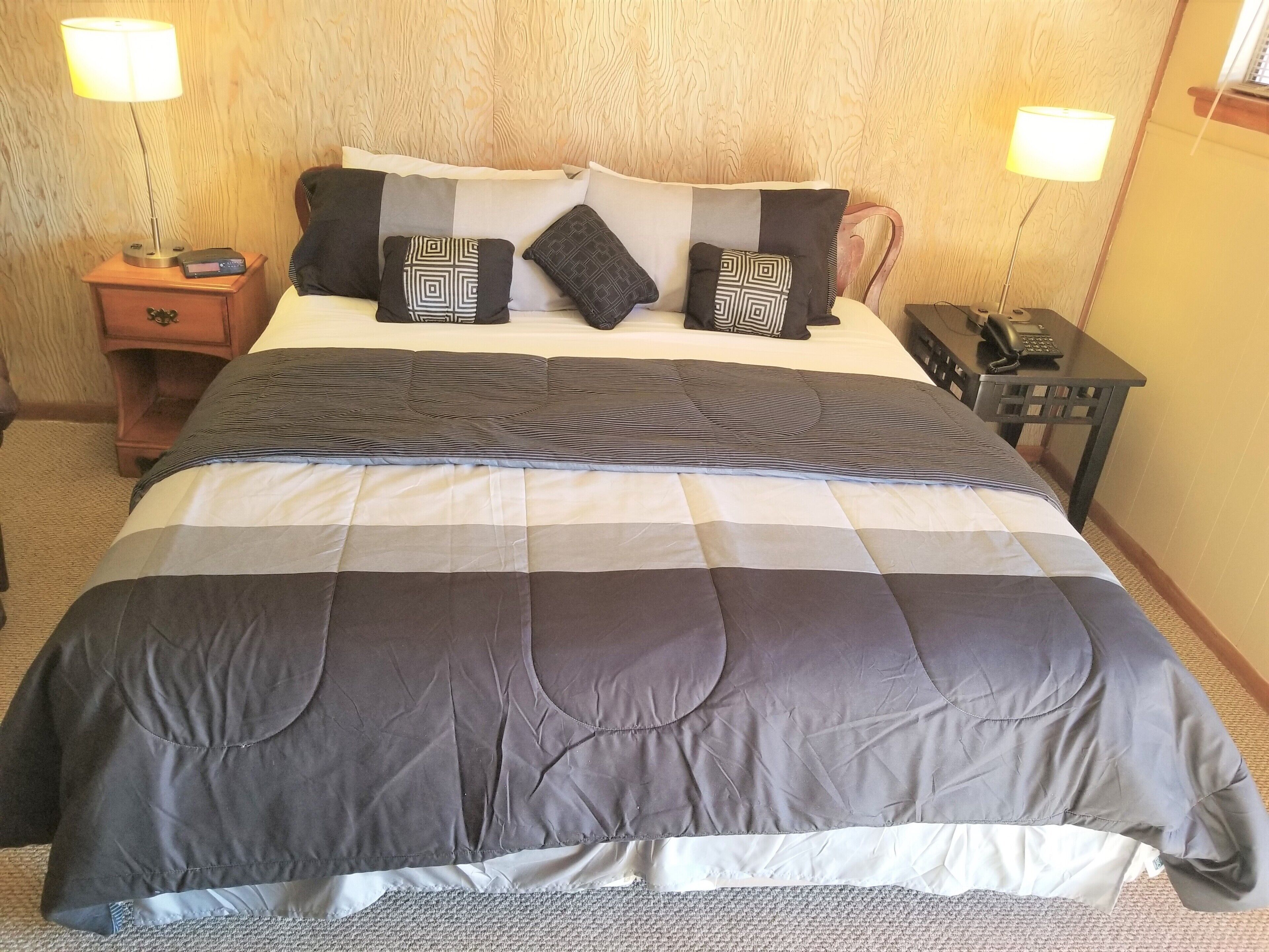 A hotel room with a large bed, two bedside tables, a nightstand, and a desk with a phone and a lamp.
