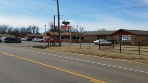 Un motel con un cartel, un estacionamiento y un área cercada con un edificio al fondo.