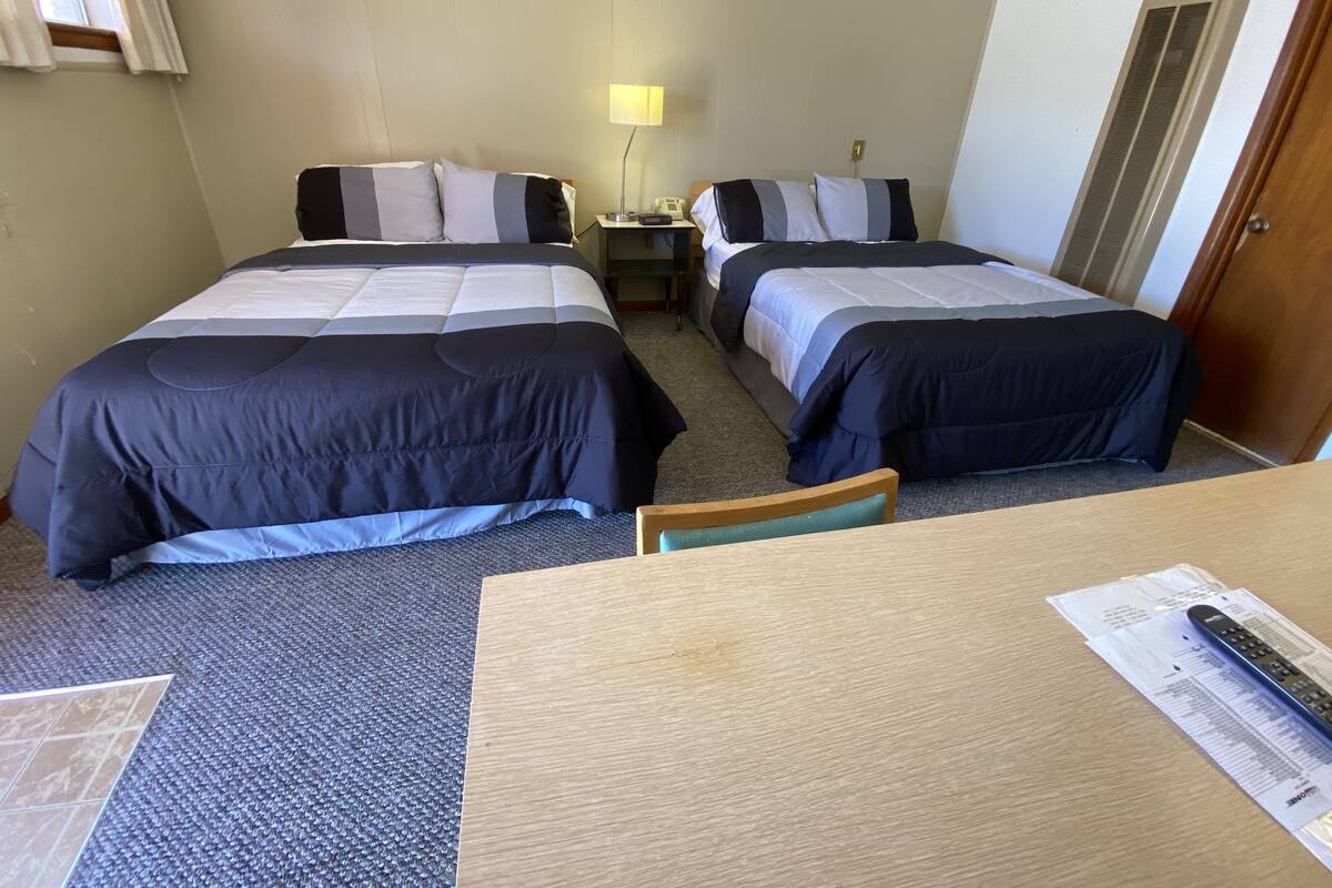 Une chambre d’hôtel avec deux lits, une petite table, une chaise, une lampe et une porte.