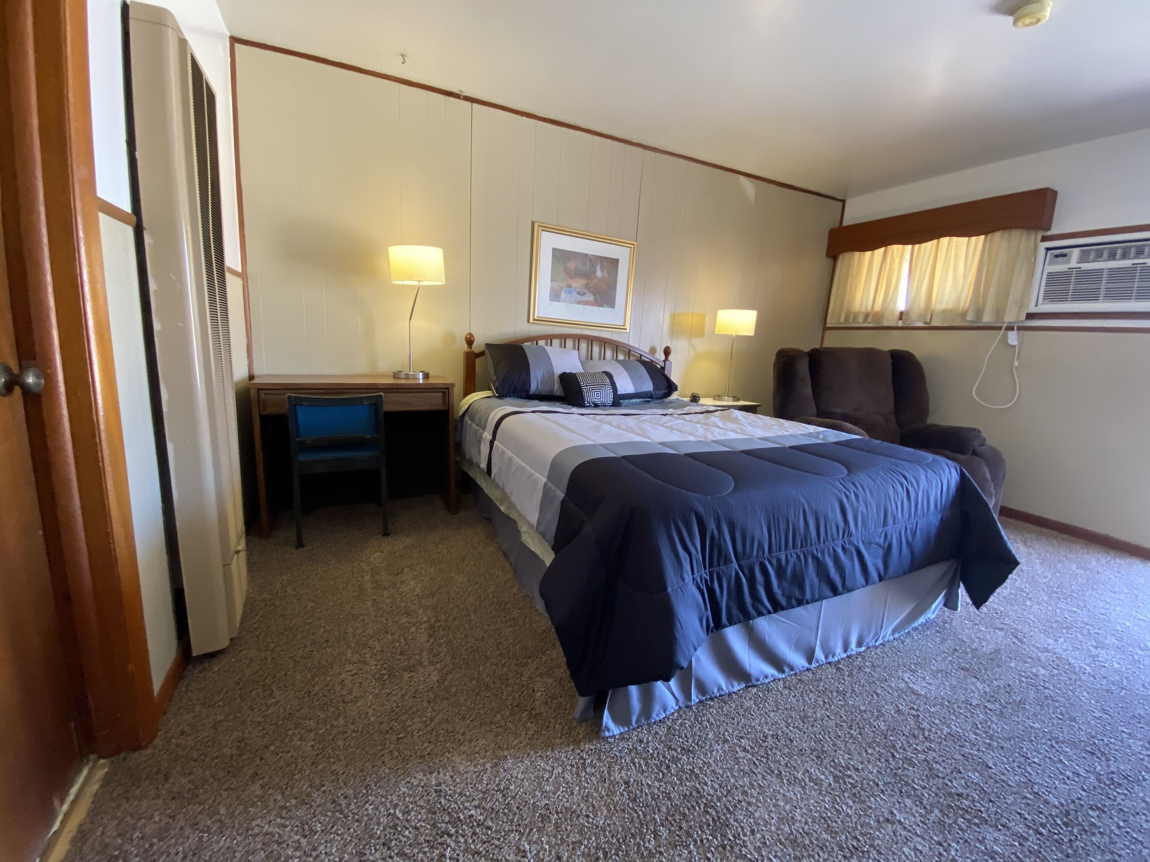 Una camera d'albergo con un letto, una scrivania, una sedia e un condizionatore d'aria.