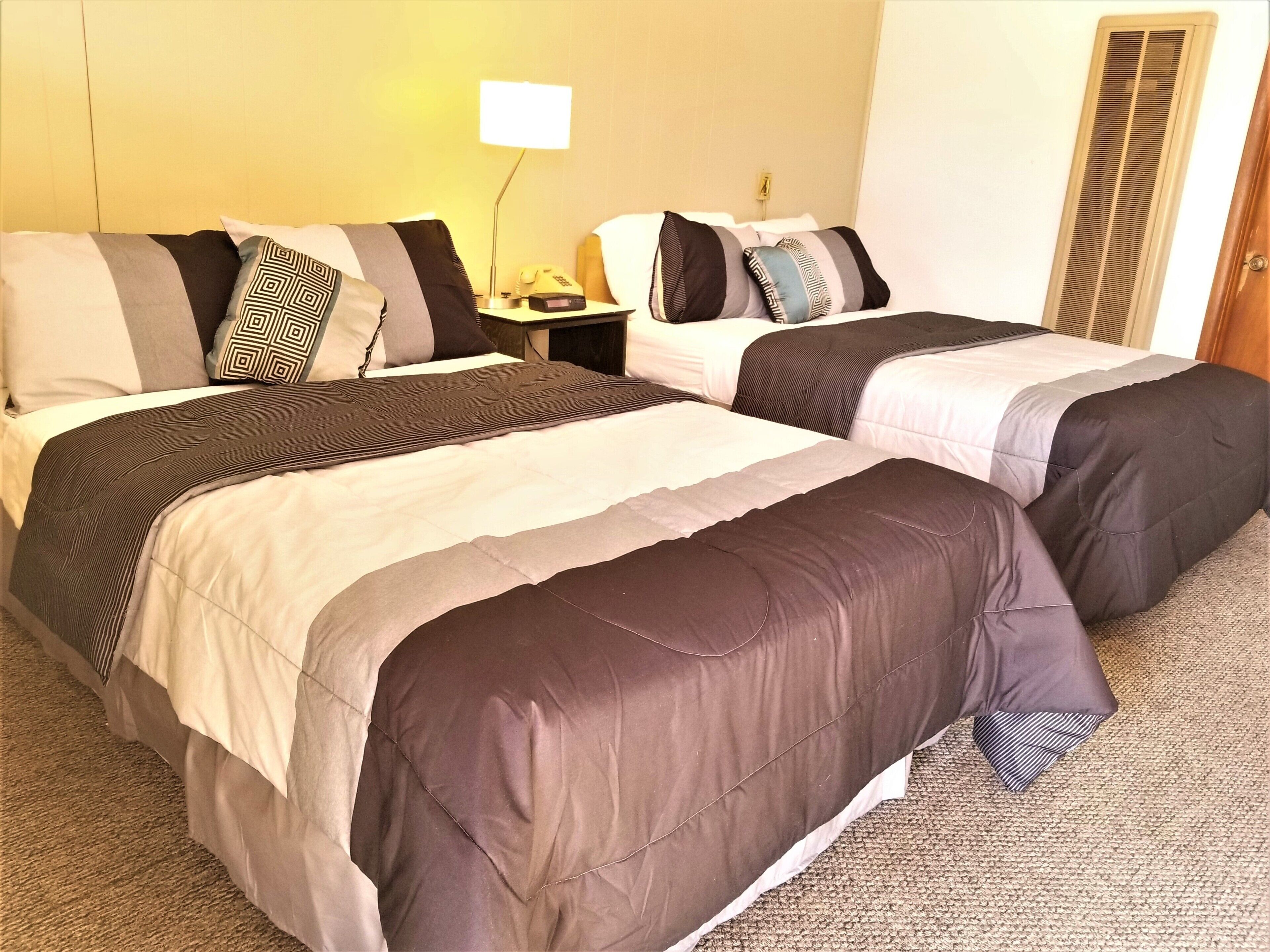A hotel room with two beds, each with a different patterned bedspread. There is a bedside table with a lamp and a telephone.