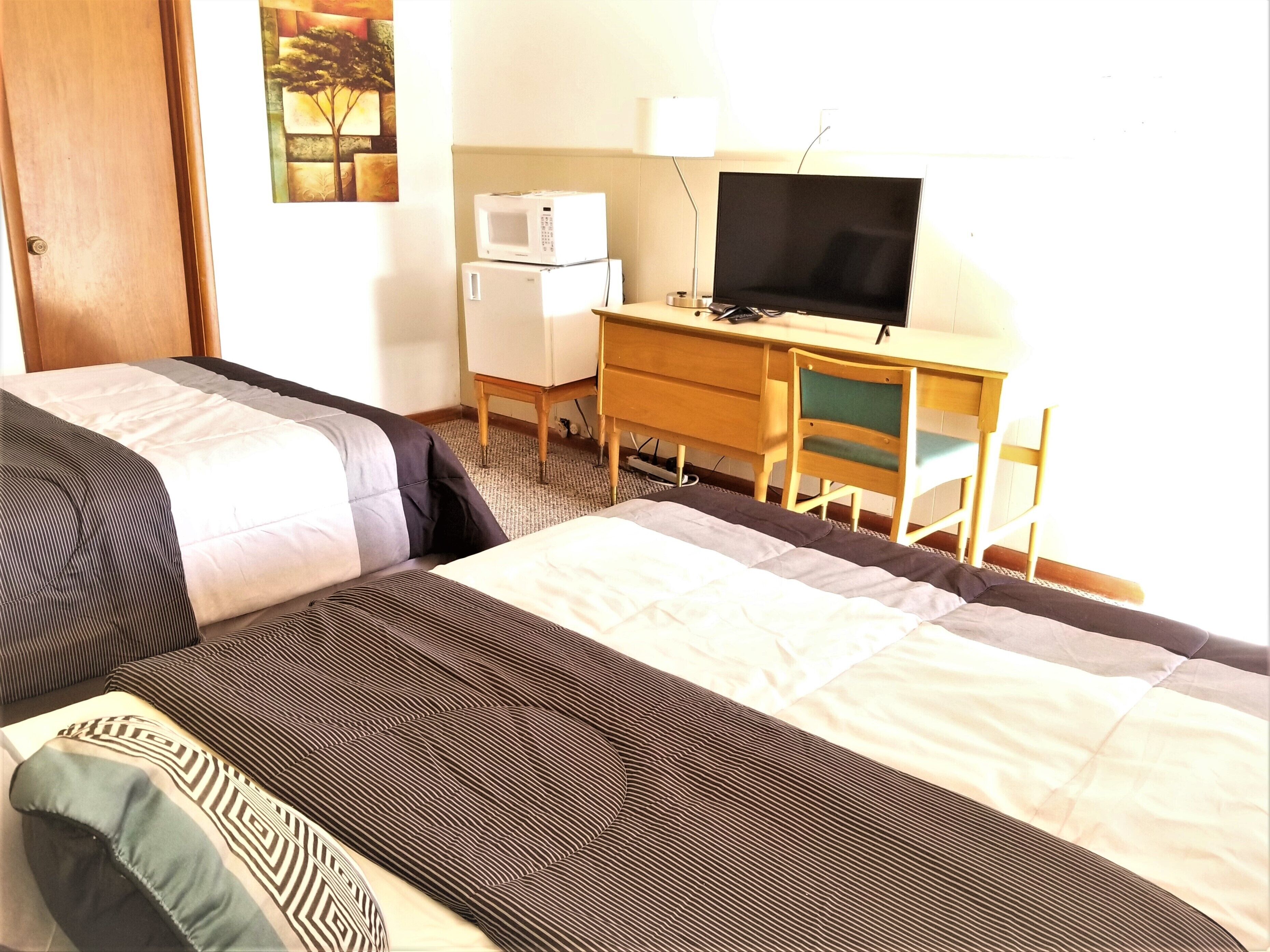 Une chambre d’hôtel équipée d’un lit, d’un bureau avec un ordinateur et une télévision, ainsi que d’un réfrigérateur.