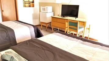 A hotel room with a bed, a desk with a computer and a television, and a refrigerator.