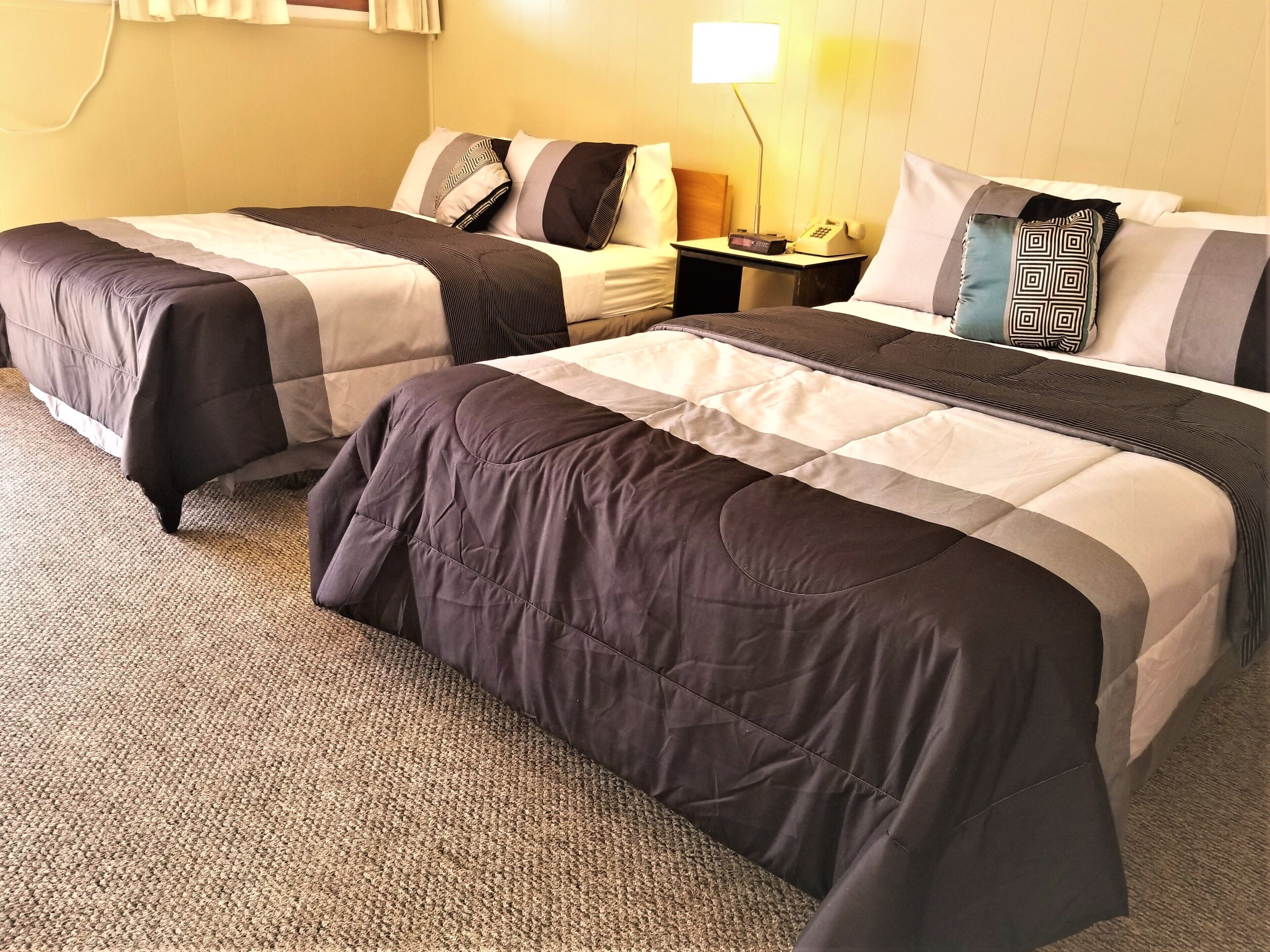A hotel room with two beds, a nightstand with a lamp, and a carpeted floor.