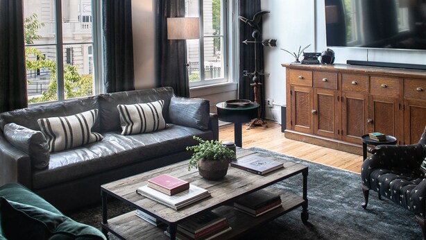 Ein modernes Wohnzimmer mit einer Ledersofa, einem Couchtisch mit Büchern, einer Chandelüster und einem großen Fernseher.