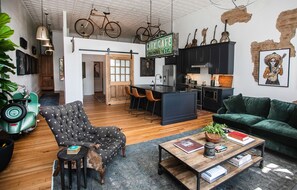 Eine moderne Küche mit Barbereich, einem Essbereich mit großem Fenster und einem Wohnbereich mit Sofa und Couchtisch.
