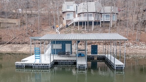 A docked houseboat with a covered deck, a small outdoor seating area, and a door leading to the interior.