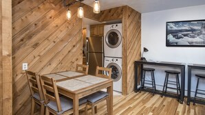 Eine kompakte Küche mit Holzwänden, einem Esstisch mit Stühlen, einer Waschmaschine und einer Bar mit Hockern.