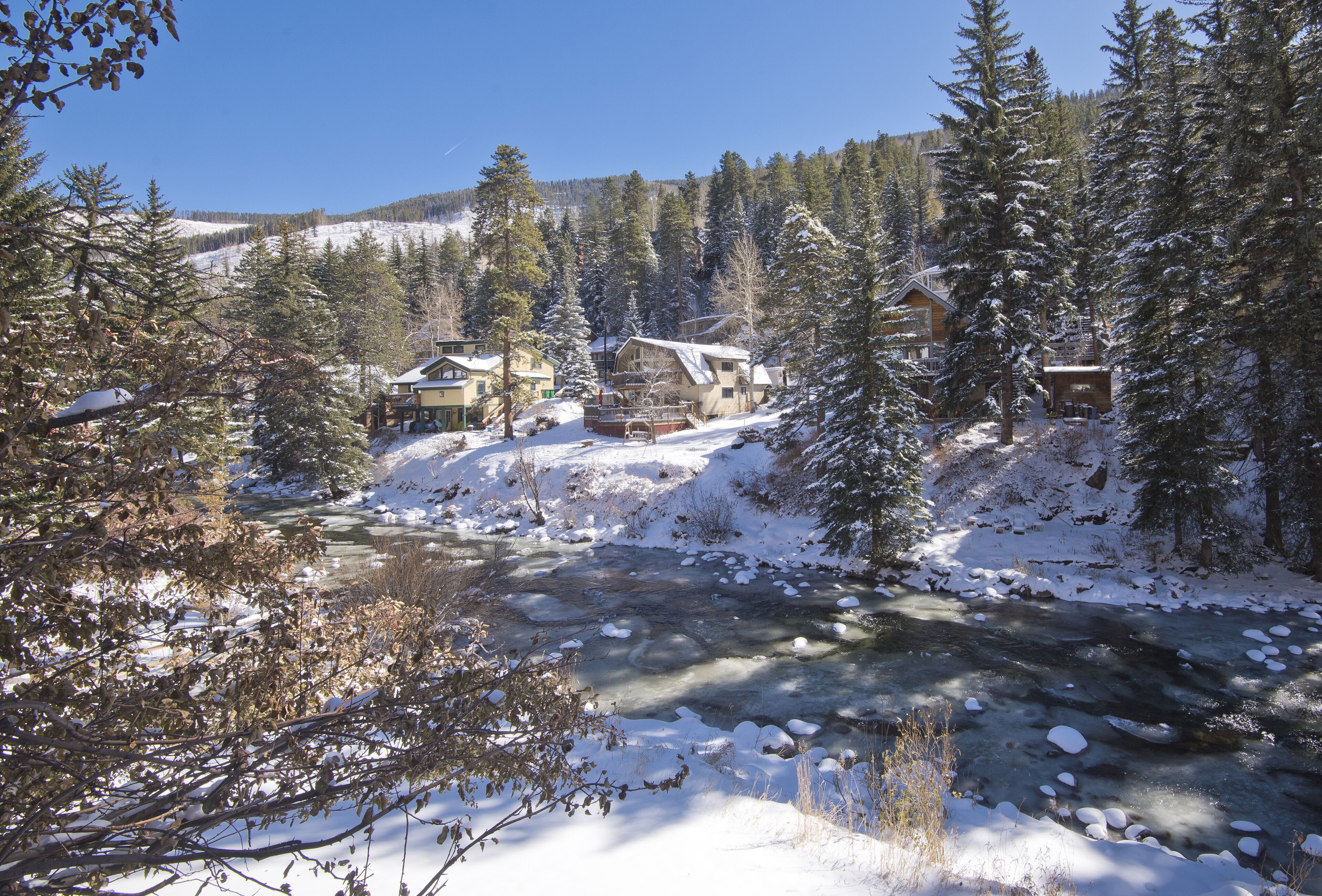 Eine schneebedeckte Lodge vor einem Fluss, umgeben von Bäumen.