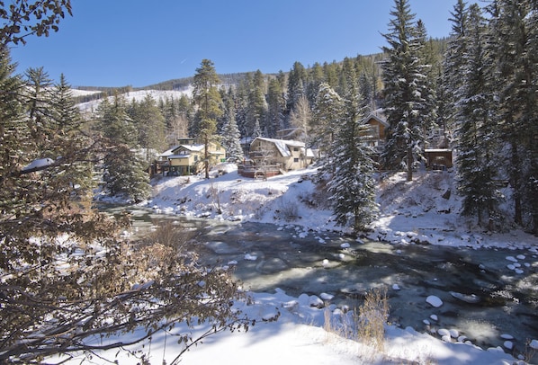A snow-covered lodge with a river in front, surrounded by trees.