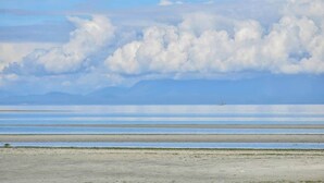 A wide, flat landscape with a calm body of water and distant mountains. - Kye Bay Winter Beach House (Comox)