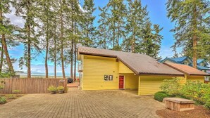 A yellow single-story house with a red door, surrounded by a wooden fence and potted plants. - Kye Bay Winter Beach House (Comox)