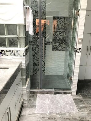 A bathroom with a glass shower enclosure, tiled walls, and a marble floor.