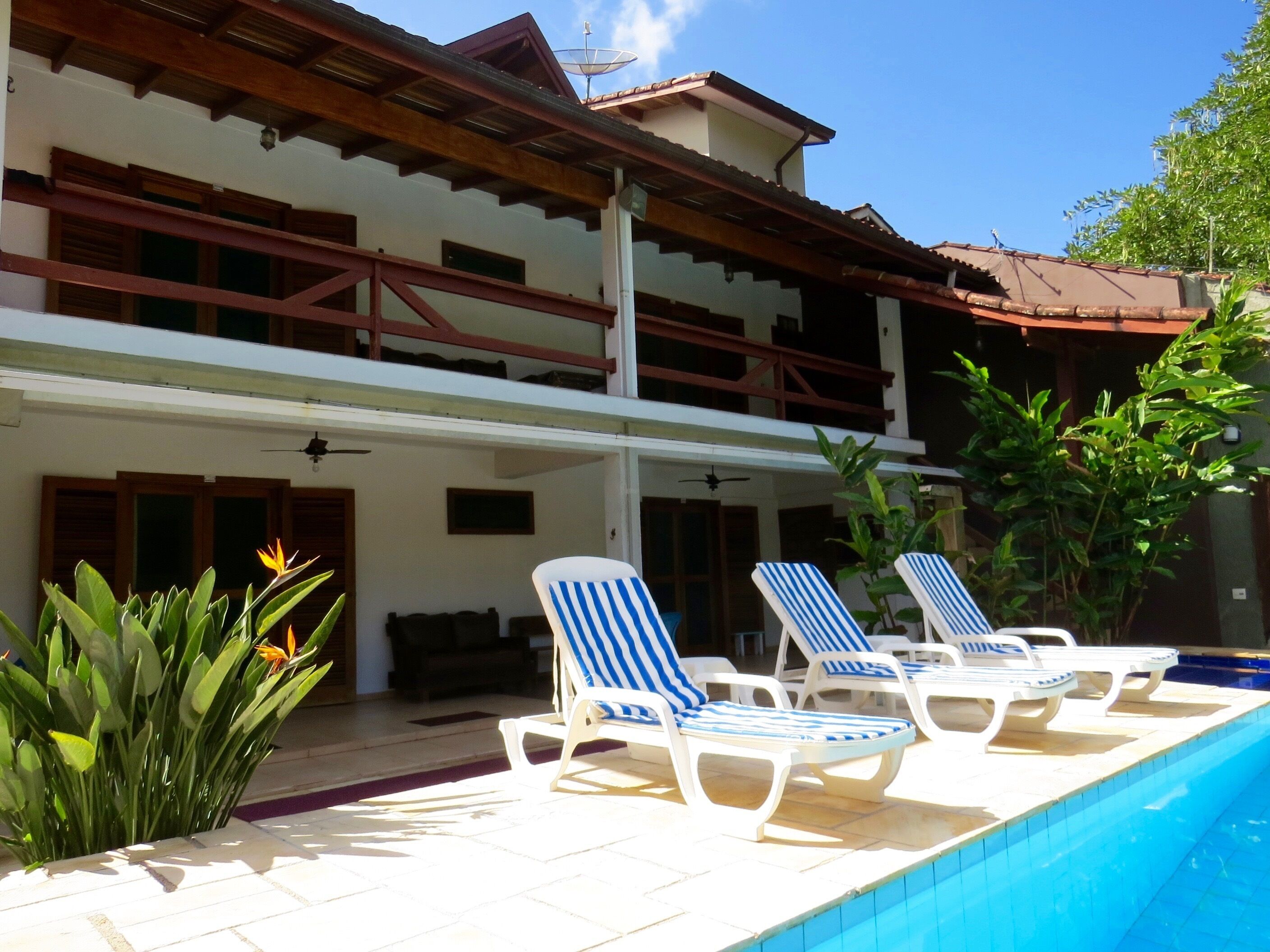 Un edificio de dos pisos con un área de piscina. Hay sillas de descanso junto a la piscina.