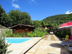 A pool area with a wooden building, a covered carport, and a mountain backdrop.