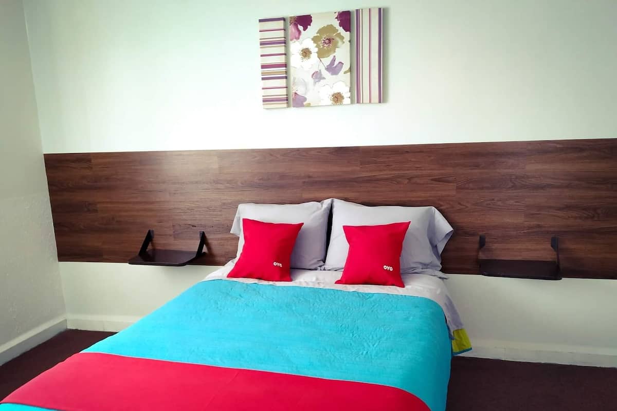 A bed with a wooden headboard, two red pillows, and a blue and red bedspread.
