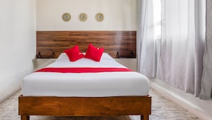 Cama bem arrumada com cabeceira de madeira, almofadas vermelhas e edredom branco.