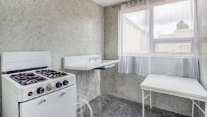 Uma cozinha compacta com fogão branco, pia pequena e branca, e janela com cortinas leves.