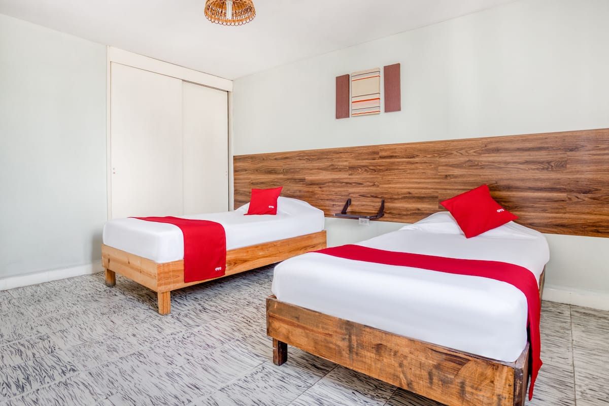A hotel room with two wooden beds, white bedding, red pillows, and a wooden headboard.