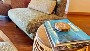 Un salon chaleureux avec un canapé vert, un fauteuil en osier et un livre intitulé « L’île de Kauai » posé sur une table ronde.
